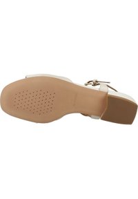 Scarpa slingback beige con suola in gomma testurizzata, tacco basso a blocco e una sottile cinghia alla caviglia con fibbia dorata.