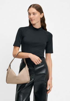 Czarny krótki top z krótkim rękawem i wysokim kołnierzem, połączony z czarnymi, błyszczącymi spodniami na wysoki stan. Modelka trzyma beżową trójkątną torebkę.