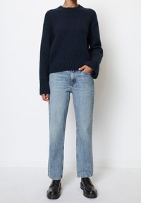Marineblauer Strickpullover mit gerippter Textur, lockerer Passform und weiten Ärmeln, kombiniert mit hellblauen, hoch taillierten geraden Jeans und schwarzen klobigen Stiefeln.