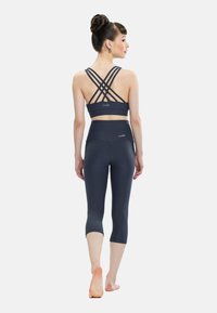 Tumši pelēks sporta krūšturis ar krusteniskām siksnām un atbilstošām kāju garuma legingām. Audums ir gluds ar pieguļošu dizainu un logotipa detaļām.