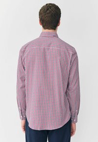 Camisa de manga larga a cuadros en rojo, azul y blanco; presenta un cuello estándar y puños con botones; tejido de algodón con una textura suave.