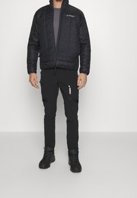 Czarna pikowana kurtka z wysokim kołnierzem i logo. Zestawiona z czarnymi spodniami z kieszeniami cargo i logo. Czarne buty trekkingowe dopełniają stylizację.