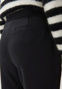 Zwarte broek met een slank ontwerp, voorzien van een discrete achterzak, gecombineerd met een gestreepte, fuzzy zwart-witte trui.