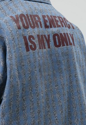 Denim shirt with a blue and grey striped pattern. Bold red text on the back reads, "YOUR ENERGY IS MY ONLY." Classic collar design.