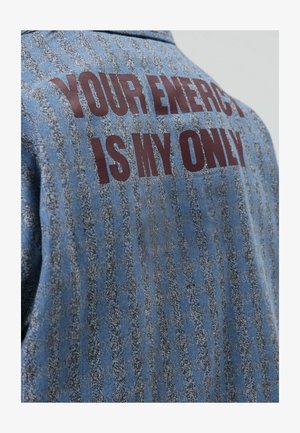 Denim overhemd met een blauwgrijs gestreept patroon. Op de achterkant staat in vetgedrukte rode letters: "YOUR ENERGY IS MY ONLY." Klassiek kraagontwerp.