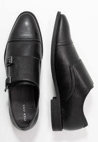 Chaussures en cuir noir avec une finition lisse, des accents à deux boucles, un bout arrondi et une semelle basse et texturée. Marque "Pier One" à l'intérieur.