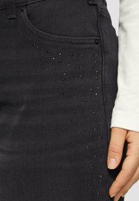 Schwarze Jeans aus Denim mit schmaler Passform, dezenten schwarzen Perlenverzierungen im Bereich der vorderen Tasche, strukturiertem Stoff und normalem Bund.