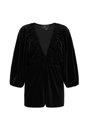 Tuta corta in velluto nero con scollo a V profondo e dettagli arricciati sullo scollo e sulle maniche. Presenta una vita elastica e pantaloncini corti.