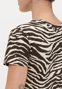 T-shirt a righe zebrate marroni e crema con maniche corte, texture a costine e scollatura rotonda. Dettagli di cucitura visibili sulle maniche.