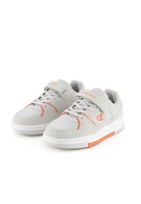 Graue Sportschuhe aus Mesh- und Wildledermaterial mit orangefarbenen Akzenten, weißen Sohlen, Schnürung und Klettverschluss.