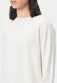 Weißer Pullover mit langen Ärmeln und rundem Ausschnitt. Weiche Textur, reguläre Passform und sichtbare Nahtdetails an den Schultern.