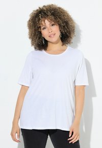 Camiseta blanca de manga corta con cuello redondo, hecha de tela suave y con un corte holgado. Combinada con pantalones negros.