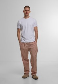T-shirt alb cu guler rotund, asociat cu pantaloni rai și albi cu dungi, având o croială lejeră și o textură moale. Pantofii slip-on maro completează aspectul.