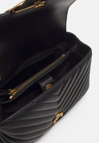 Zwarte leren handtas met een gequiltte textuur, voorzien van een gouden rits en hardwareaccenten. Het interieur bevat een ritsvak voor organisatie.