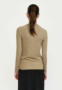 Khaki színű, hosszú ujjú felső, bordázott anyagból készült, kerek nyakkivágással és testhez álló fazonnal, fekete szoknyával párosítva.