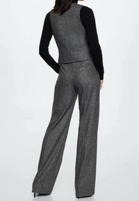 Gilet en tweed gris et pantalon à jambes larges, caractérisés par une coupe ajustée, un tissu texturé, et une chemise noire à manches longues contrastante en dessous.