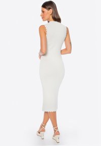 Witte, geribbelde midi-jurk met gegolfde randen, mouwloos ontwerp, getailleerde silhoutte, gecombineerd met crèmekleurige sandalen met straps.