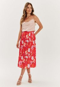 Volná midi sukně v jasně červené barvě s růžovým květinovým vzorem, spárovaná s hedvábným růžovým topem. Má tenké ramínka a volný střih. Sandály na podpatku.