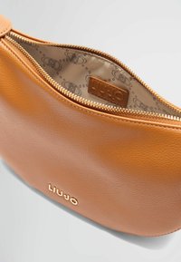 Geantă din piele maro deschis cu o textură netedă, având un fermoar auriu și un logo embosat. Interior căptușit cu un material cu un model în tonuri neutre.