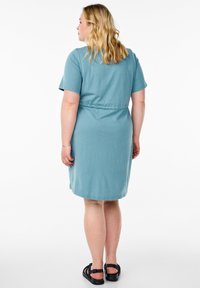 Robe à manches courtes, longueur genou en coton teal clair avec une taille cintrée et une silhouette décontractée. Associée à des sandales noires.