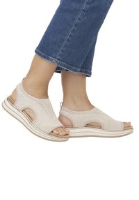 Beige knitted sandals featuring open-toe design, elastic straps, and cut-out details. Thick sole with a textured bottom for grip.