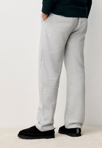 Pantalon de survêtement gris en tissu doux avec une coupe décontractée, doté de poches latérales et porté avec des chaussures noires basses à enfiler.