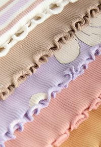 Pièces de tissu côtelé empilées en beige, lavande, rose et crème, chacune avec des bords ondulés et froncés et des motifs subtils.