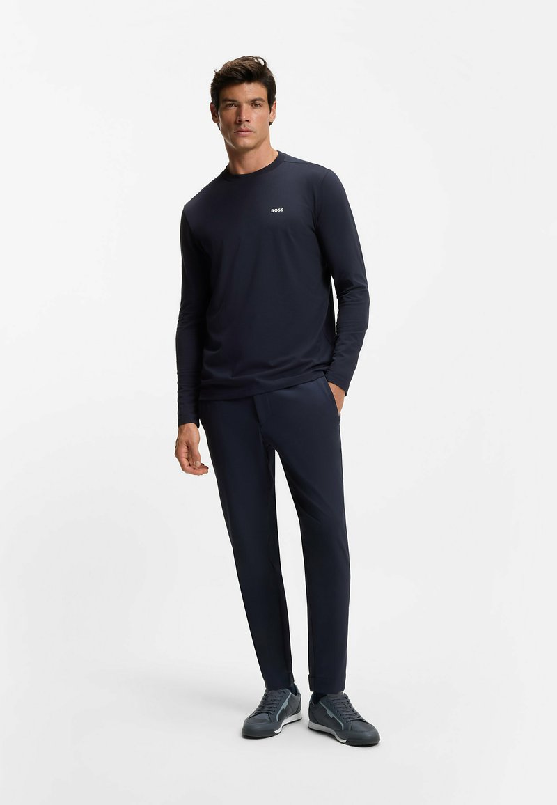 Laivastonsininen pitkähihainen paita, jossa on huomaamaton logo, yhdistettynä samanvärisiin kapeisiin housuihin ja tummaansneakereihin. Sileä kangas, moderni muotoilu ja istuva leikkaus.