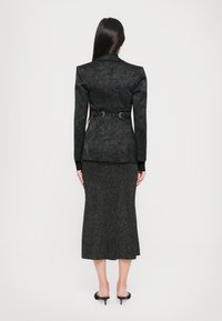 Black patterned blazer with a structured design and a fitted waist, paired with a textured, knee-length black skirt. Heels visible.