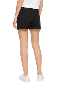 Zwarte denimshorts met opgerolde pijpen, voorzien van achterzakken en een hoge taille. Gemaakt in combinatie met witte sneakers, gezien vanaf de achterkant.