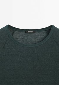 T-shirt ribbed verde scuro con scollo rotondo e maniche raglan. L'etichetta riporta "Massimo Dutti", indicando l'origine del marchio. Tessuto morbido.