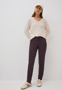 Un pull léger beige en V associé à un pantalon de jogging violet foncé avec une taille élastique et un cordon de serrage. Baskets blanches avec des accents.
