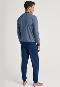 Heren loungewear-set bestaande uit een blauw gestreepte longsleeve top met geribbelde manchetten en bijpassende effen blauwe broek met enkelmanchetten.