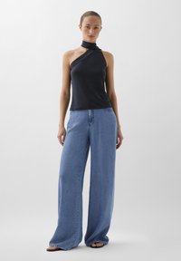 Zwarte mouwloze top met asymmetrische halslijn, gecombineerd met lichte spijkerbroek met wijd uitlopende pijpen. Gladde textuur, casual ontwerp en geen zichtbare patronen.