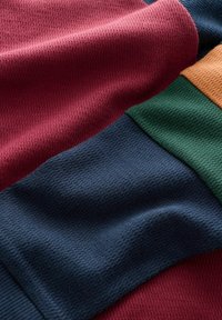 Textured fabric layers in burgundy, navy, green, and mustard, showcasing varying knit patterns and smooth finishes.