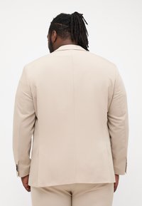 Beige tailored suit jacket with a smooth texture, single vent at the back, and buttoned cuff details. Suitable for formal occasions.