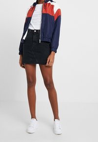 Veste légère à blocs de couleurs bleu marine et rouge avec capuche, associée à une jupe en denim noire et des baskets blanches ; dotée de poignets et d'une ceinture élastiques.