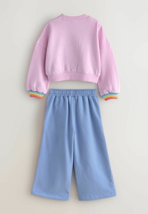 Rosa, verkürzter Pullover mit Regenbogenstreifen an den Bündchen und hellblauen, weiten Hosen mit elastischem Taillenbund. Weiches Baumwollmaterial.
