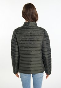 Jachetă căptușită de culoare verde închis, cu guler înalt. Are un design capitonat și o textură netedă, prezentată din spate purtând blugi slim-fit.