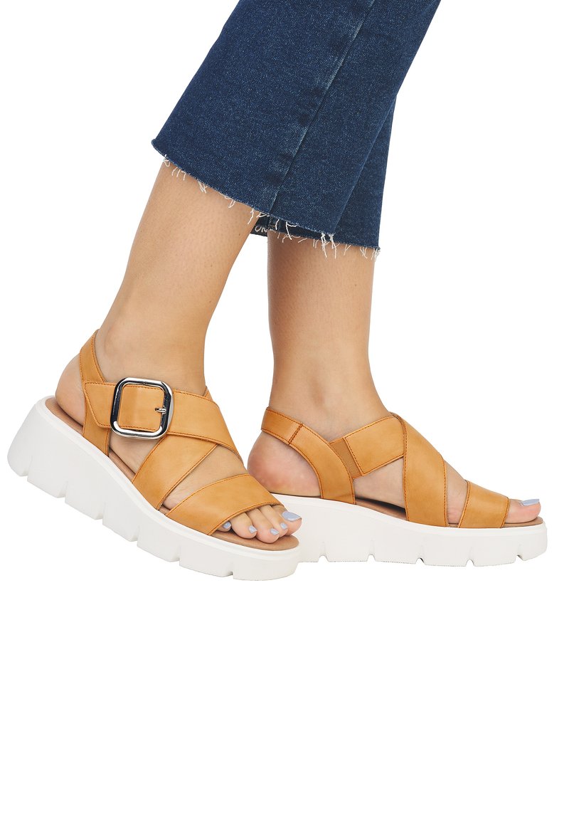 Sandales en cuir tan avec des brides croisées et une grande boucle en argent. Elles ont une semelle plate-forme blanche épaisse et un design à bout ouvert.