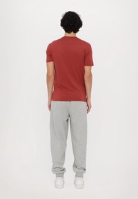 Czerwona koszulka z krótkim rękawem i okrągłym dekoltem, zestawiona z luźnymi, szarymi spodniami dresowymi i białymi trampkami, widziana od tyłu.