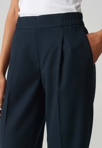 Pantalons ajustés bleu marine avec une taille structurée, des plis et des poches latérales, dotés d'un tissu texturé.