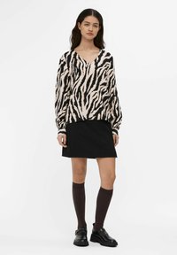 Sort og beige zebra-stribet bluse med lange ærmer og V-hals, parret med en sort nederdel og brune knæhøje sokker; sorte klumpede sko.
