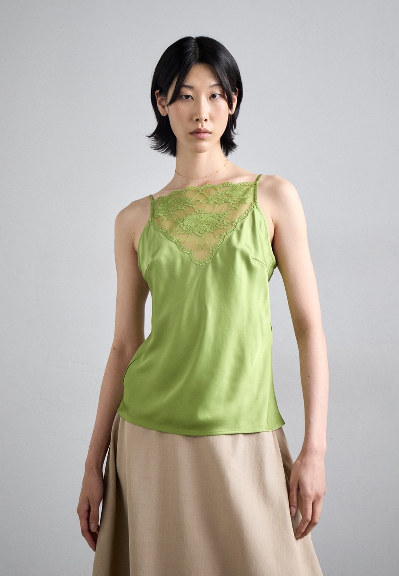 Green satin camisole featuring lace detailing at the neckline, thin straps, and a soft, smooth texture. Paired with a beige skirt.