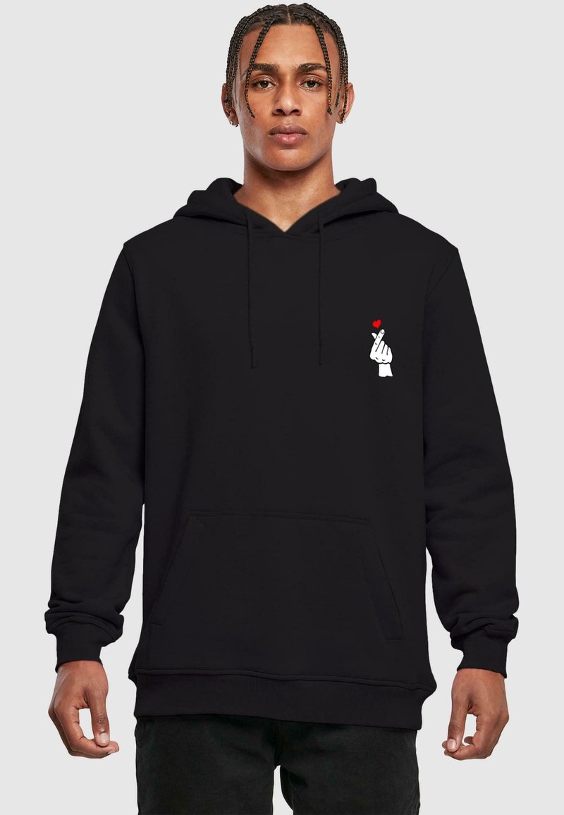 Black hoodie with a front pocket, featuring a white hand graphic with a small red heart. Material appears soft and textured.