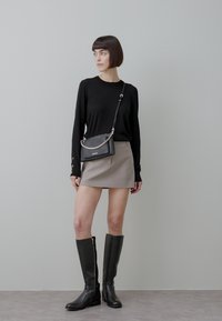 Juoda ilgarankovė palaidinė, smėlio spalvos mini sijonas, juoda per petį nešiojama rankinė su grandinėle, juodi kelio aukščio batai su užtrauktukais, modernus minimalistinis stilius.
