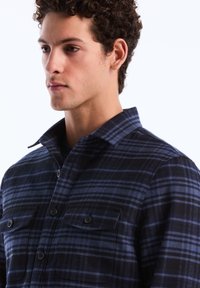 Karierte Flanellhemden in Schwarz und Blau, mit einer Knopfleiste vorne, spitzem Kragen und zwei Brusttaschen mit Knopfverschluss.