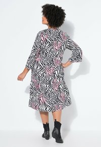 Vestido de manga larga con volantes en estampado de cebra blanco y negro, con detalles en rosa, combinado con botines negros adornados con tachuelas plateadas.