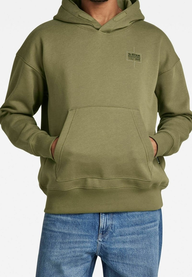 Felpa verde oliva in cotone, con tasca frontale, polsini a costine e una piccola toppa con logo sul petto. Design a vestibilità classica.