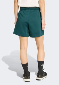 Teal, mid-thigh length shorts with an elastic waistband; made of soft material; paired with black athletic shoes and ribbed black socks.